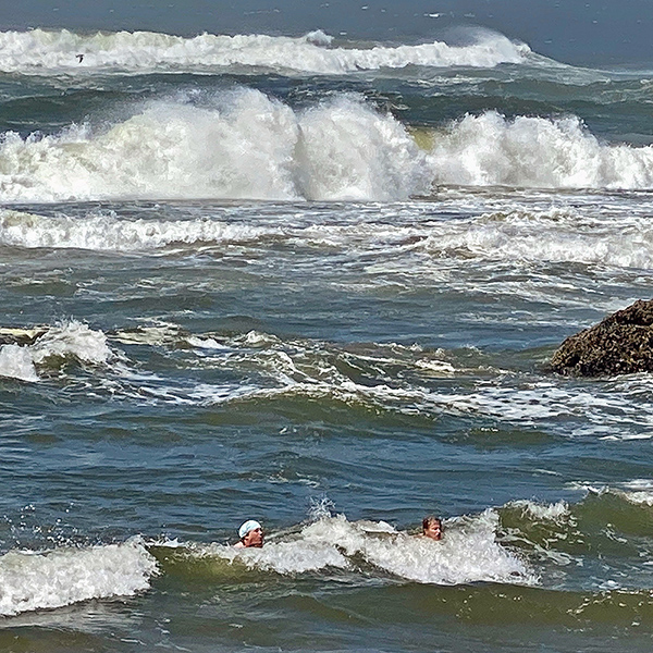 Eric and Jennell in a wave. Eric is wearing a blue cap to protect his head from sunburn.