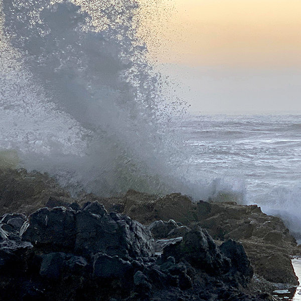 Waves crash into the rocks and spray high up into the air.