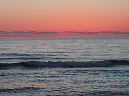 Pink dawn sky before sunrise with dark waves on the coast