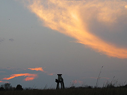 Dramatic clouds over the prairie meadow and an interesting sculpture on the horizon