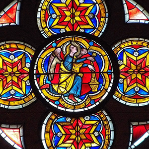An angel with a blue robe and yellow coat holds a censor with insense while kneeling and looking up toward Christ