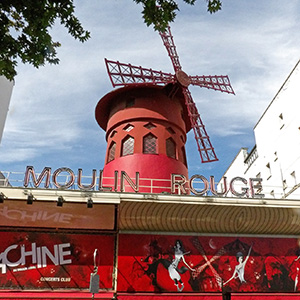 The red windmill stands above a mural on the front of the building showing people dancing.