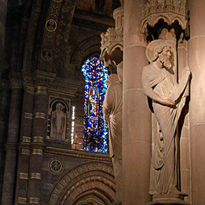 Statue inside the cathedral with stained glass behind it