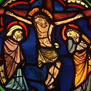 Jessu hangs on the cross, with his eyes shut. On either side of him stand figures who are in great distress.