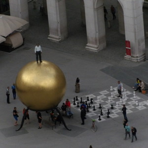 People playing chess by the golden ball with a man on the top in Kapitelplatz square in Salzburg.