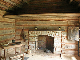 a stone fireplace and a wooden table in the modest log cabin.