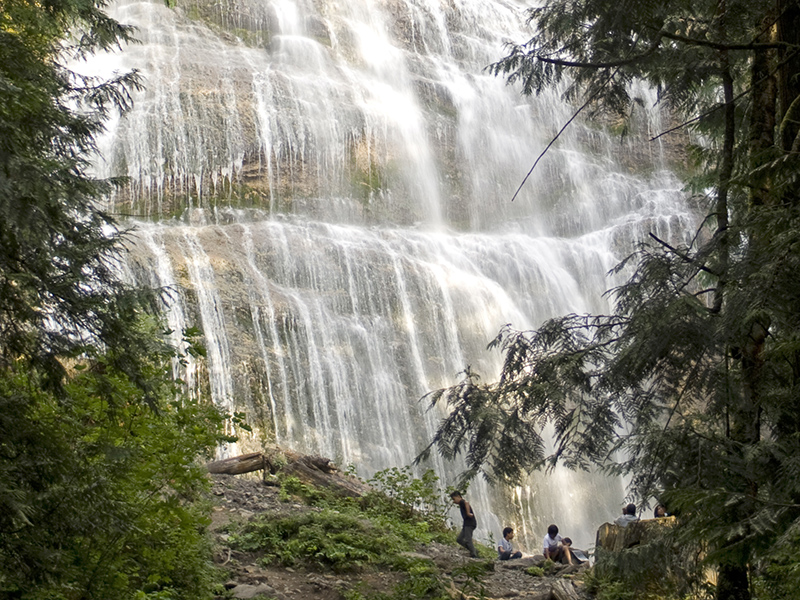 A view of Bridal Falls from a distance, with people at the base looking very small in comparison to the falls