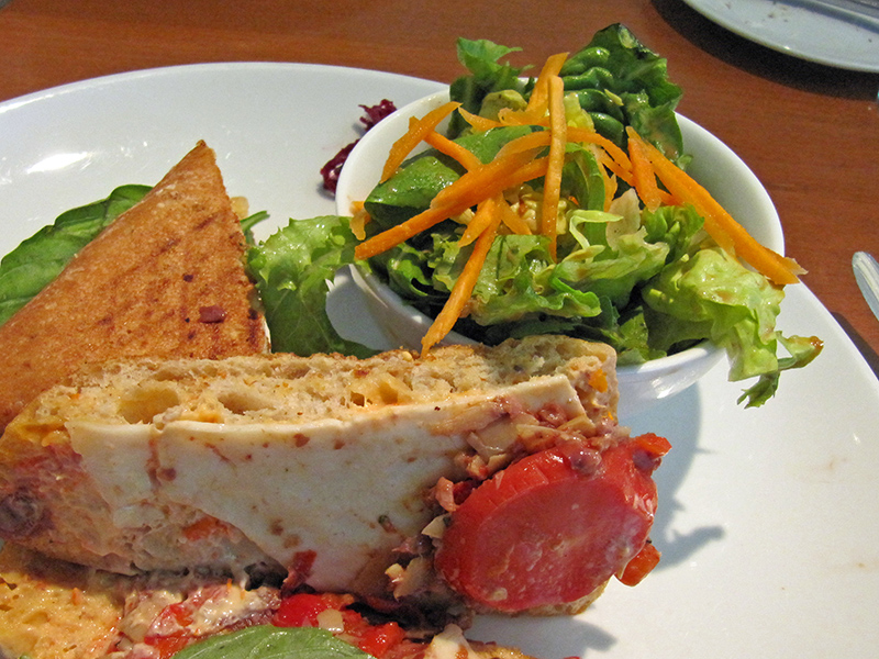 The white plate holds a small salad and a cheese sandwich with tomato and other ingredients