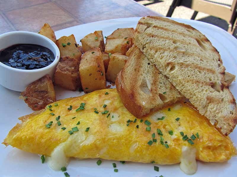 Cheese oozes out of folded egg omlet with toast and fried potatoes on a plate
