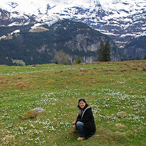 Jeri is crouching in a meadow with many white crocus blossoms around her and the snow-covered Jungfrau in the background.
