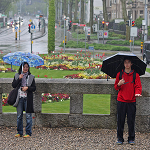 Jeri and Arthur are standing in the rain holding their umbrellas, with the flowers of Saint Paul Church behind them