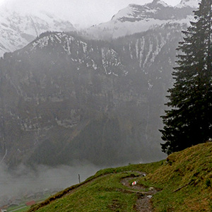 The trail winds along the slope with great mountains shrouded in mist across the valley