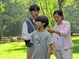 Two cute boys and their mom with sunlight shining through leaves behind them.