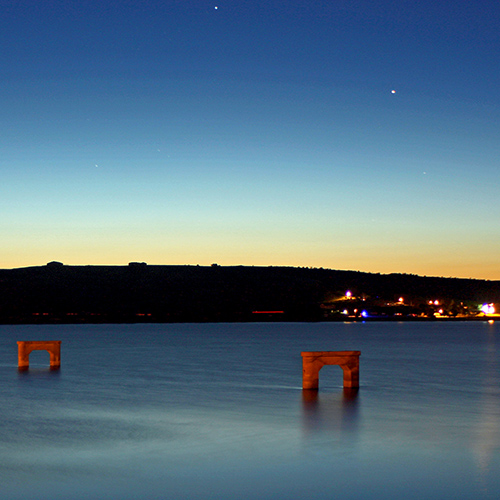 Two stars in the dark sky with a glow from the setting sun over the hills.