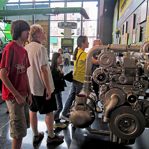 A display of engines against a wall, and people are looking at them and reading the information about them on signs