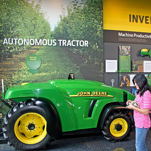 A rather small tractor with a rounded front end sits in front of a photograph of an apple orchard.