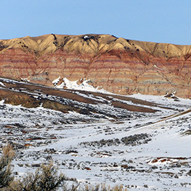 The colorful stones of fossil lakebeds give color to a bluff that rises above the snowy country at Fossil Butte