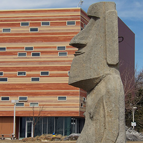 A reproduction of a Moai from Easter Island is sitting in front of a modern building on the campus of Western Wyoming College