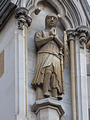 A knight wearing chain mail stands with his hands clasped in prayer