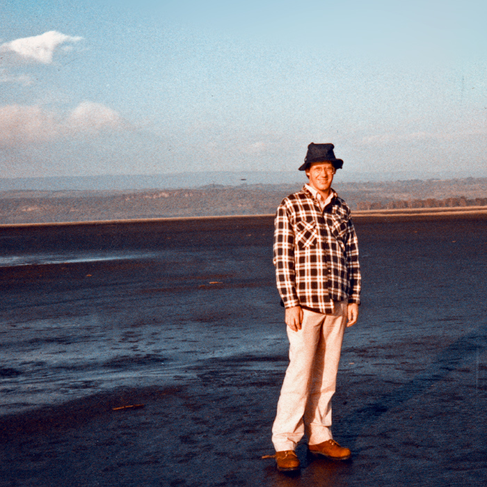 IEric standing on a muddy flat area with a lake and hills fading in the distant haze behind him