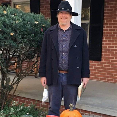 Eric stands behind table of candy, wearing a black hat and coat