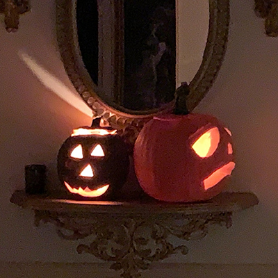 Pumpkin lanterns in a hallway in front of a mirror, with candle light coming out of the lanterns