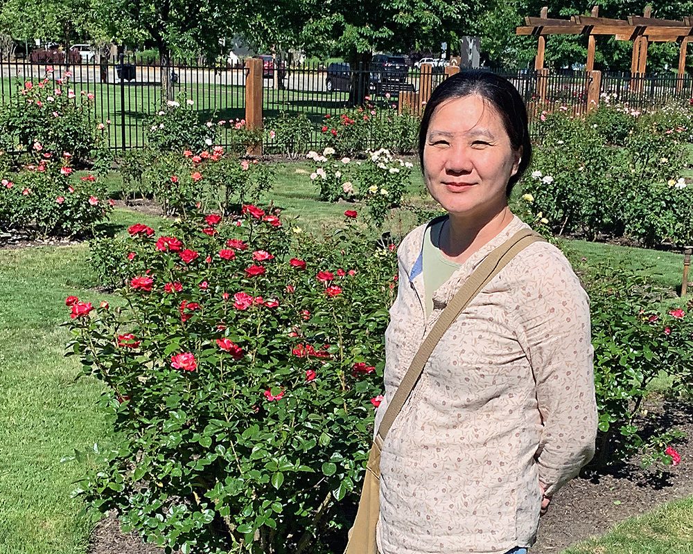 Jeri in Julia Davis Park, Boise. She is standing and smiling, and behind her are some roses.