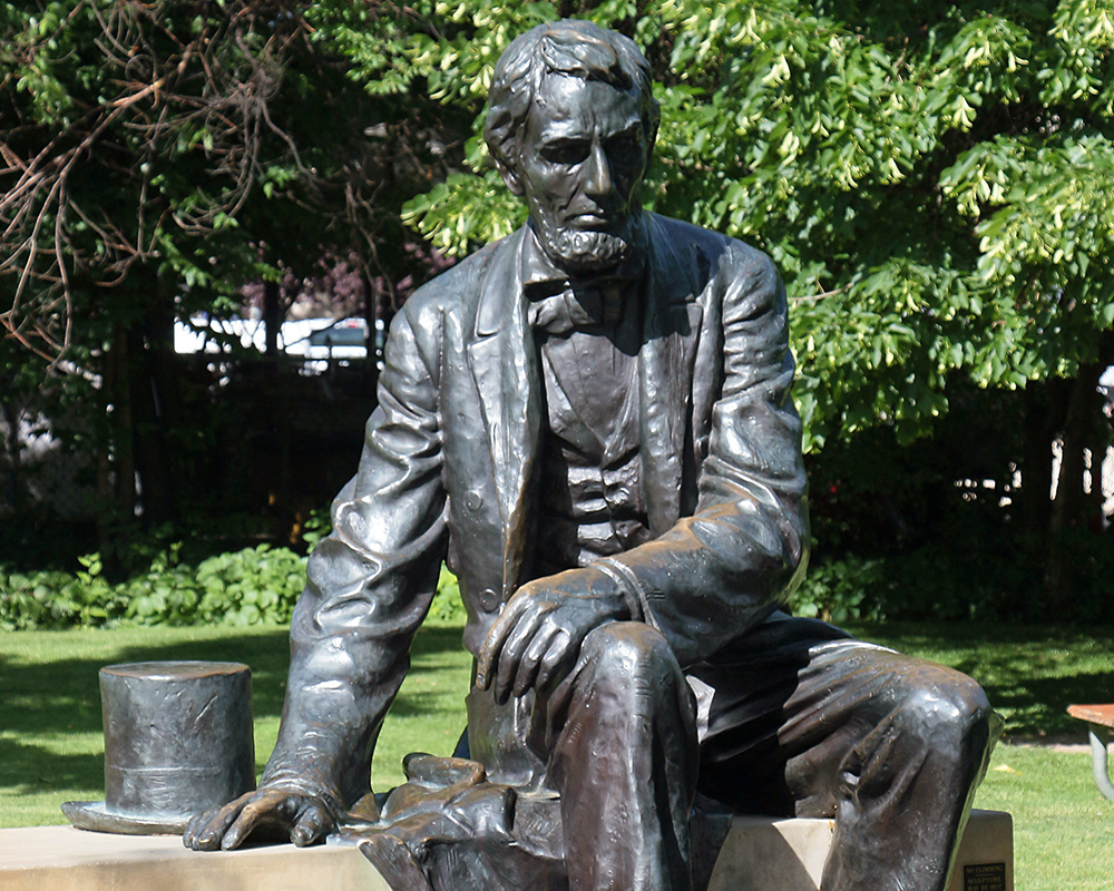 Statue in Bronze of Abraham Lincoln sitting on a bench with his top hat by his side.
