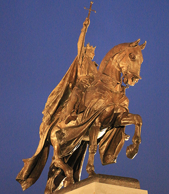 Saint Louis is dressed as a knight with a crown and riding a horse