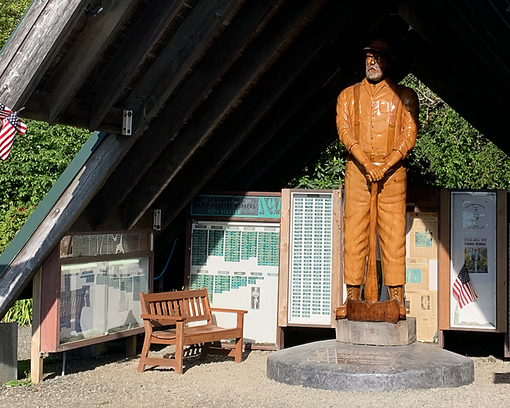 Loggers Memorial has a wooden carved statue of a logger under a steep-roofed shelter.