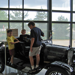 Three children climbing in a very old car inside the Family Museum