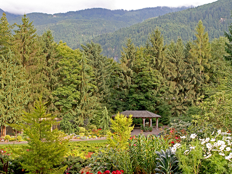 A pavilion in a garden with trees as a backdrop, and mountains in the near distance behind