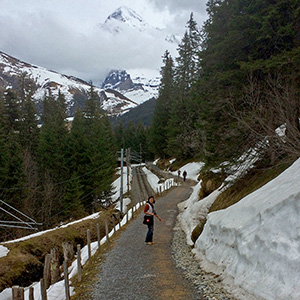 Jeri is walking on a trail with a tall mountain peeking out of the clouds behind her